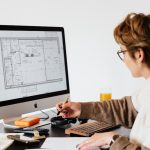 Side view of anonymous female employee in casual clothes and eyeglasses writing out information from computer while working at table in modern light office