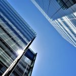 Low angle view of glass skyscrapers reflecting the bright sun in a clear blue sky.