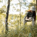 A teenager explores a forest using a magnifying glass, surrounded by sunlight and wildflowers.