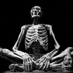 Black-and-white image of a skeleton sculpture in a meditation pose, emphasizing anatomy.