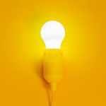 Illuminated light bulb with a vibrant yellow background, symbolizing ideas and inspiration.