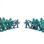 Green toy soldiers facing off on a white background, symbolic of conflict and strategy.