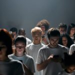 A diverse crowd focused on smartphones, illustrating social isolation and technology connection.