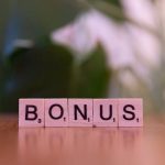 Close-up of the word BONUS spelled with Scrabble tiles on a table.