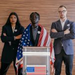 Diverse group of political candidates standing with American flag at voting podium.