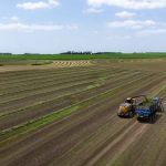 Aerial view of tractor harvesting crops in expansive farm fields under a clear sky.