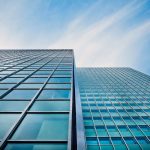 A low angle view of a modern glass skyscraper against a clear blue sky.