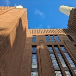 Dynamic perspective of a historic brick industrial building against a clear blue sky.