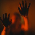Mysterious silhouette of hands on frosted glass with dramatic red lighting.