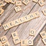 Wooden letter tiles arranged on a wooden surface spelling out 'healthy', symbolizing wellness.