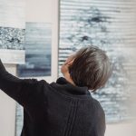 A woman arranges abstract art pieces on a gallery wall, showcasing modern creativity.