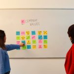 Two women in an office discussing company values on a whiteboard.
