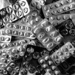 Black and white image of pill blister packs scattered on euro bills and coins.