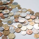 A diverse collection of international coins spread across a white surface, showcasing various currencies and designs.