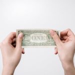 A close-up image of hands holding a one dollar bill, symbolizing finance and economy.