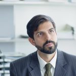 Thoughtful businessman in suit and tie in modern office environment.