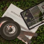 A flat lay of vintage films, a newspaper, and a tablet on grass.