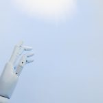 A robotic hand reaching towards a bright light on a white background symbolizing innovation.