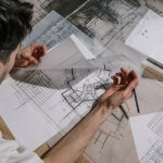 Architect studying and sketching over detailed architectural blueprints indoors.