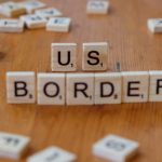 Scrabble tiles spelling 'US Border' on a wooden surface, symbolizing immigration themes.
