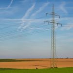 High voltage power line standing tall in a vast agricultural field under a clear blue sky in Germany.