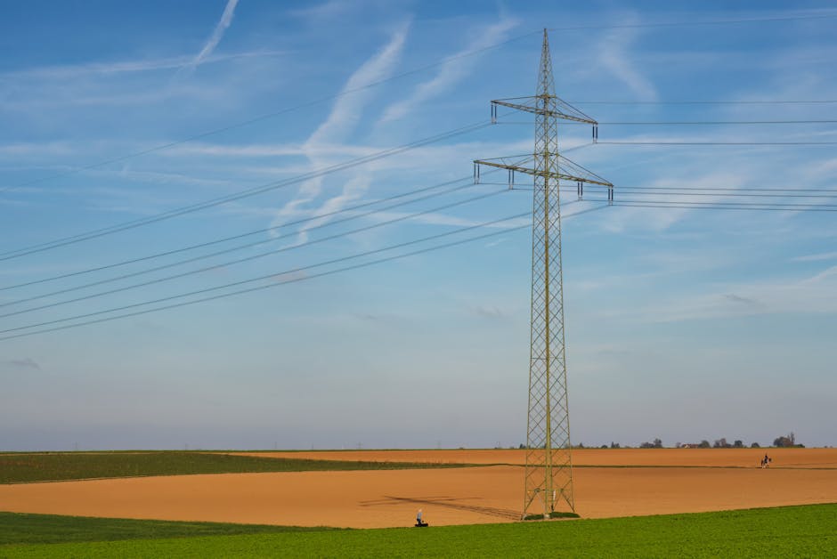 High voltage power line standing tall in a vast agricultural field under a clear blue sky in Germany.