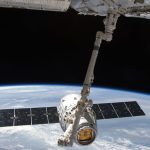 View of a spacecraft docked at the ISS above Earth with visible solar panels.