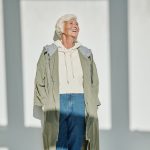 Senior woman smiling while wearing a chic coat and jeans, embracing modern fashion with a joyful expression.