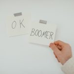 A hand holding a sticky note with the popular phrase 'OK Boomer', illustrating generational dialogue.