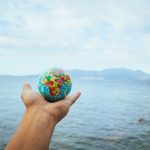 A hand holds a small globe with a scenic ocean backdrop, symbolizing global exploration.