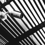 Black and white CCTV camera capturing geometric shadows under a modern structure.