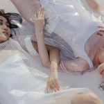 Stylish portrait featuring two young women lying in artistic, transparent fashion attire. Modern and conceptual.