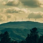 Wind turbines on a hill under a dramatic cloudy sky, showcasing renewable energy amidst nature.