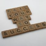 Wooden tiles spell 'Fail Your Way to Success' emphasizing perseverance.
