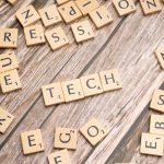 Wooden Scrabble tiles spelling 'TECH' on a textured surface, showcasing creativity.