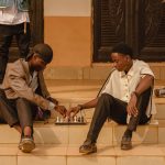 Two young men playing chess on steps outdoors in Ado Ekiti, Nigeria.
