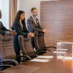 A diverse group of professionals discuss around a ballot box in a conference room.