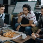Group of young men having pizza and discussing ideas during a startup meeting in a casual setting.