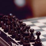 Close-up of black chess pieces aligned on a chessboard, ready for play.