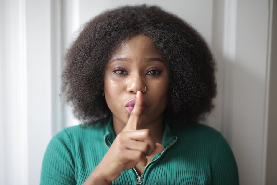 Portrait of a woman with afro hair signaling silence by holding a finger to her lips.