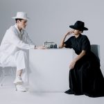 Stylish chess game between a man and woman in monochrome outfits, focusing on strategy and contrast.