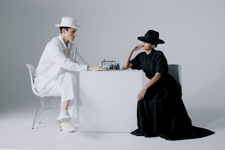 Stylish chess game between a man and woman in monochrome outfits, focusing on strategy and contrast.