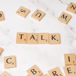 Wooden Scrabble tiles on a marble background spelling 'Talk', symbolizing communication and language.