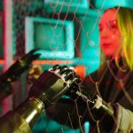 A woman interacts with robotic hands through a mesh displaying a neon cyberpunk atmosphere.