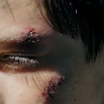 Intense close-up of a young person's face with visible wounds reflecting survival.