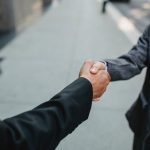 Close-up of two businessmen shaking hands outside, symbolizing partnership and agreement.