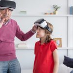 A senior man and young girl explore virtual reality together indoors.