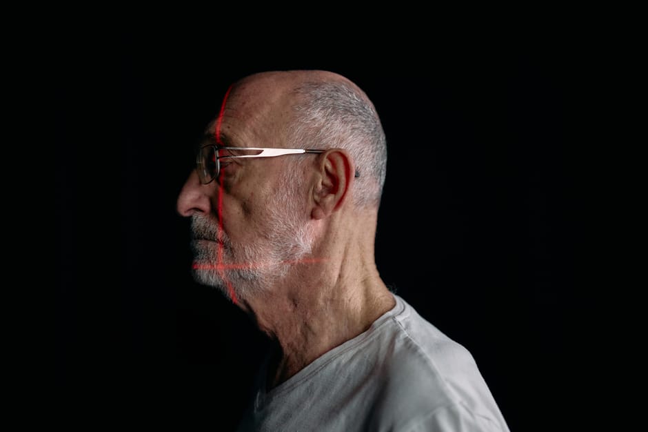 Side profile of a senior man with facial recognition scan lines on a plain black background.