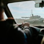 View from inside a car driving past a military tank on a road in Ukraine.