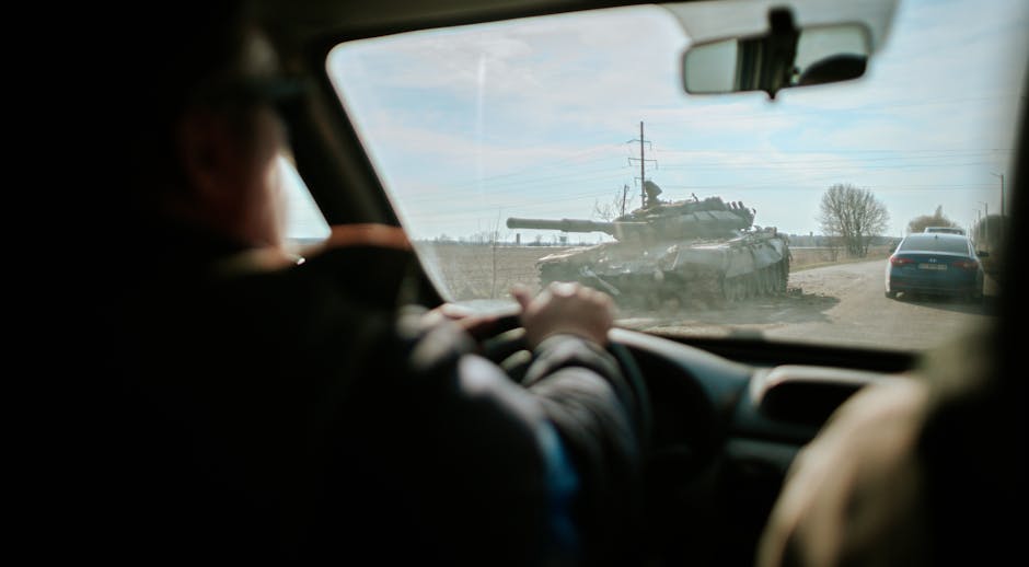 View from inside a car driving past a military tank on a road in Ukraine.
